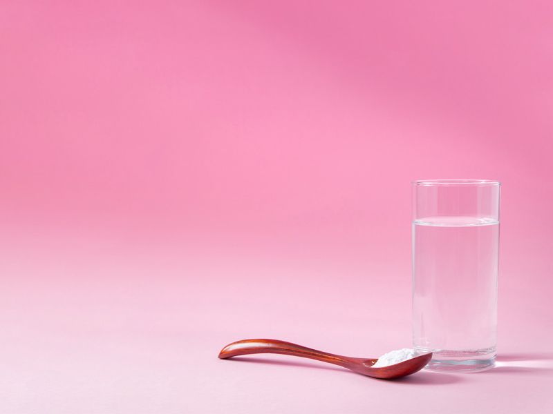 Glass of water and wooden spoon full of mixing powder on pink gradient background