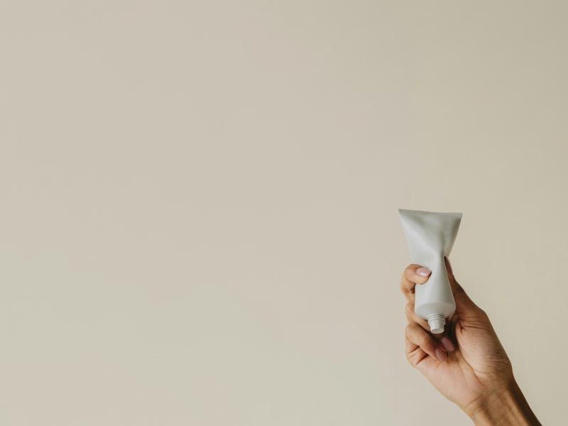 A person's hand holding a white tube in front of a beige background