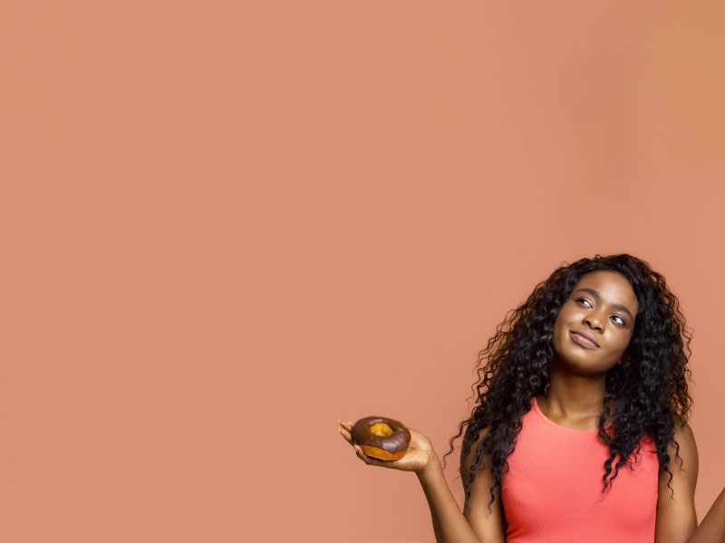 A pretty woman wearing a red shirt looks contemplative while holding a donut