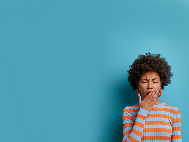 Woman in striped sweater yawning with teal background