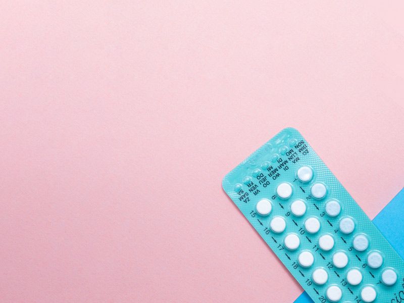 A blue birth control packet on a pink and light blue background