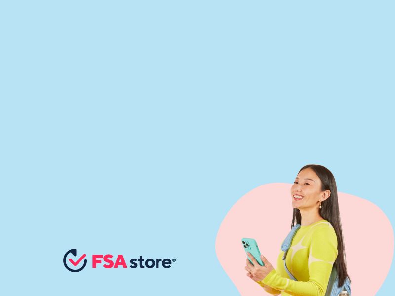 A woman wearing a bright green sweater, orange pants and a light blue backpack is smiling while holding a mobile phone