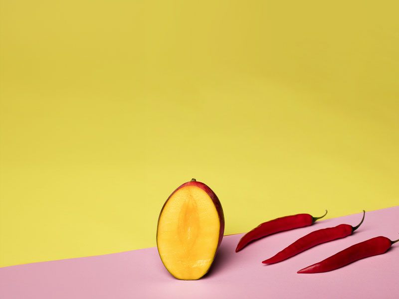 Cut open fruit and red peppers on a yellow and pink background