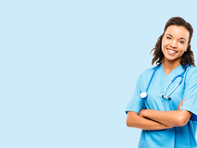 A female medical professional who is smiling and wearing blue scrubs and a stethoscope