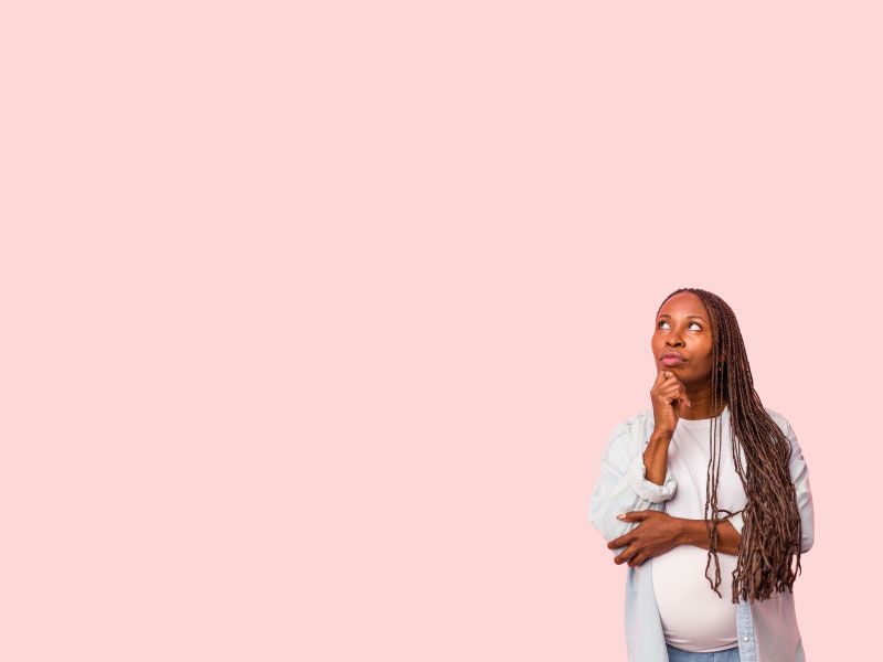 A pregnant woman wearing a white shirt is looking contemplative in front of a pink background