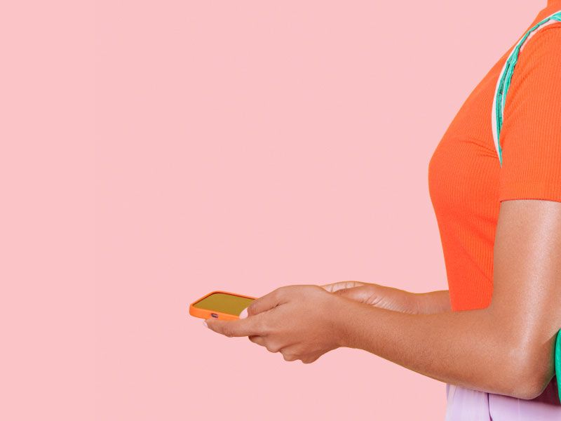 Woman carrying back of Wisp medication and holding a phone on a pink background