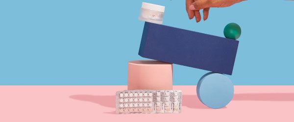A Wisp glass pill jar and 4 birth control packets are balanced on colorful abstract shapes on a pink surface with a blue background