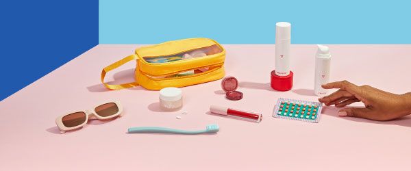 Various Wisp products, a yellow travel bag, sunglasses, a toothbrush, lip gloss and a birth control packet are laid out on a pink surface with a blue background