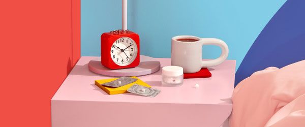 A Wisp glass pill jar and 2 emergency contraception packets are on a pink nightstand with a red alarm clock and white mug next to a bed with colorful bedding