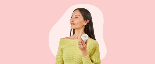 A woman wearing a bright green sweater looks proud while holding a Wisp pill vial in front of a pink background