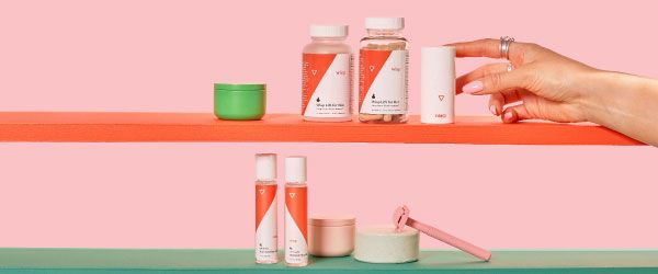 Various Wisp products on colorful shelves with a pink razor and misc containers and a woman's hand reaching for OMG Cream in front of a pink background