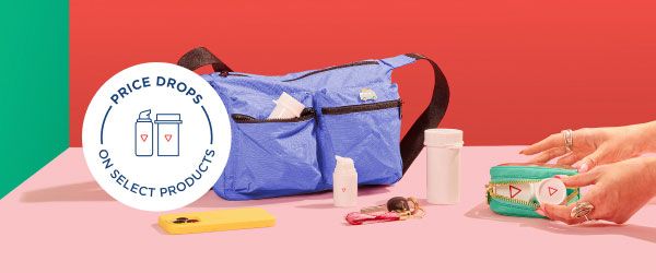 A woman's hands grabbing Wisp medication vials from a travel pouch sitting on a pink surface with a mobile phone, keys and a larger travel bag
