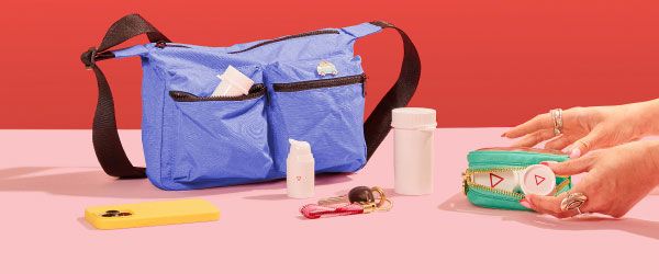 Various Wisp products on a pink surface with a blue travel back and a green travel pouch, a yellow mobile phone and keys on a pink surface with a red background
