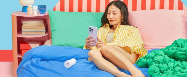 A woman laying on a bed with colorful bedding using a mobile phone next to a nightstand with Wisp medication bottles