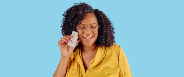 A woman wearing a yellow shirt is holding a bottle of Wisp supplements with a pill in her mouth