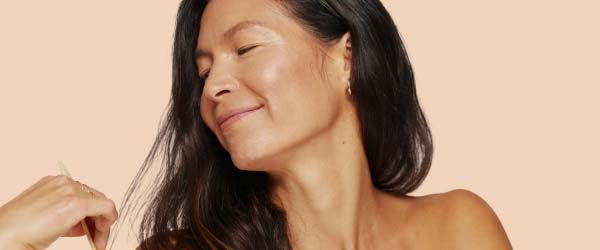 A smiling woman with glowing skin and dark hair with a cream background