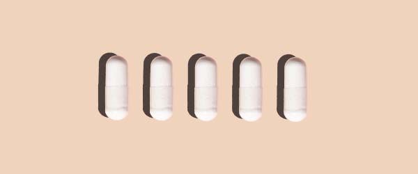 5 white capsules on a beige background