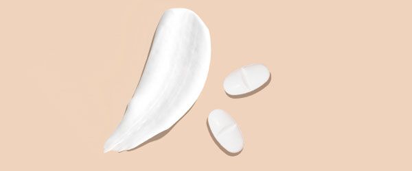 A cream swatch and two white pills on a cream surface