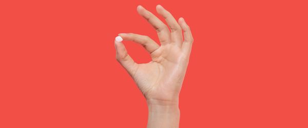Hand holding fluconazole pill for same-day yeast infection treatment on a red background