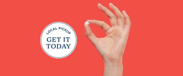 Hand holding fluconazole pill for same-day yeast infection treatment on a red background