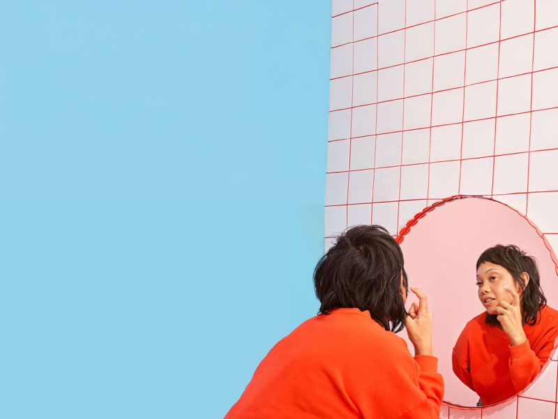 A woman looking into a mirror with a red frame on a white and red tile wall