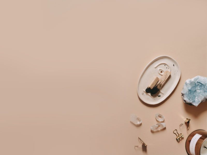 A tray with burnt palo, gemstones and a candle on a tan surface