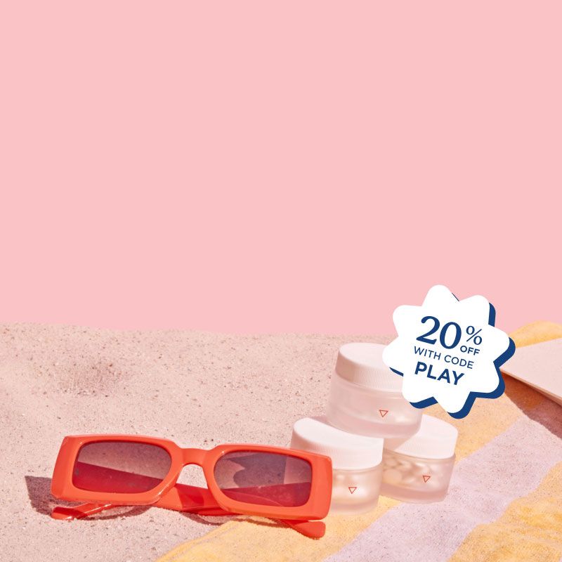 3 stacked Wisp jars and red sunglasses on a pink and yellow striped beach towel on sand