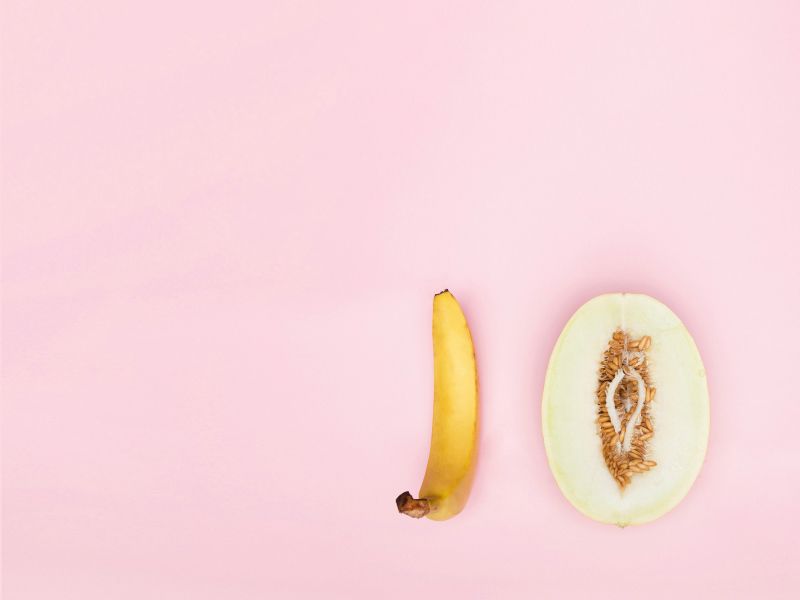 A suggestive cut open fruit and a banana on a pink background