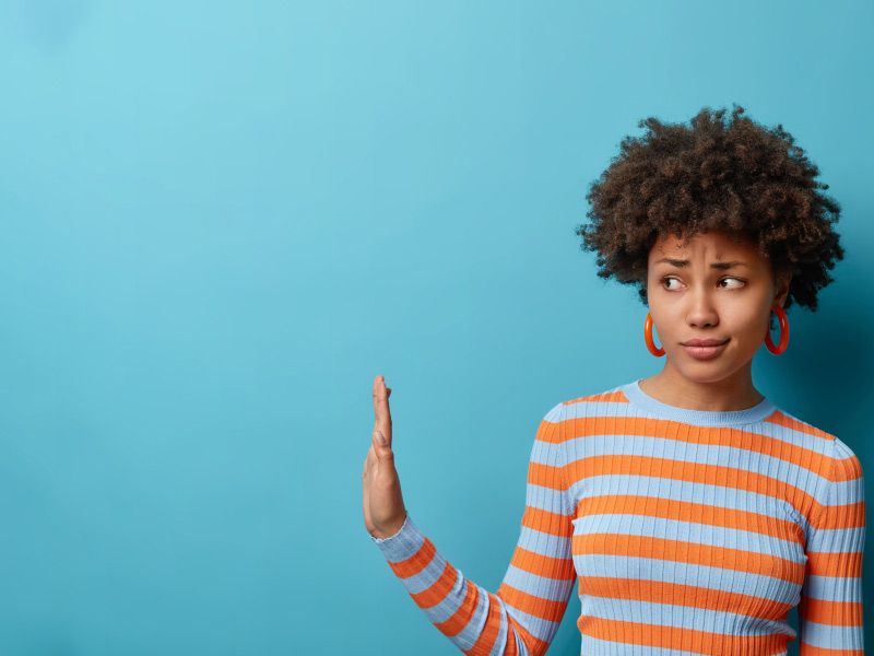A woman in a striped sweater raises her hand and gives side eye on a blue background