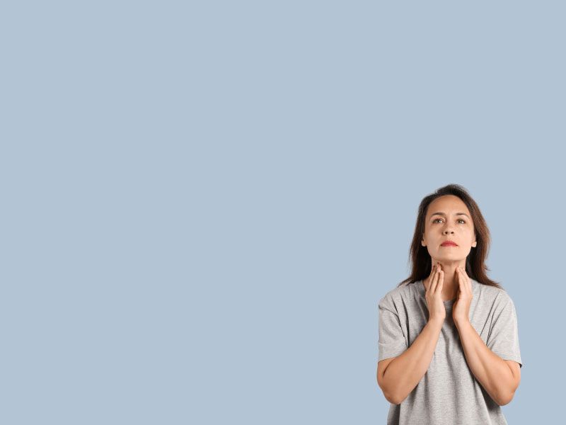 A woman wearing a gray shirt has her hands on her neck checking her thyroid