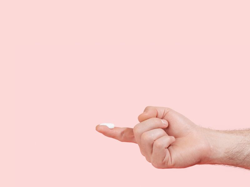 Man's hand with lidocaine cream on the index fingertip with a pink background