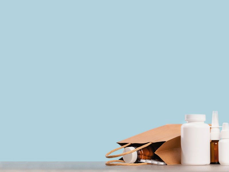 Various medication bottles and a paper bag with medications spilling out on a gray surface with a green background