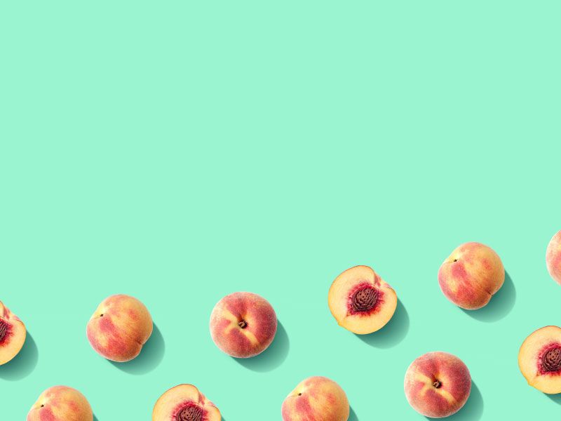 Whole and halved peaches laid out in rows on a bright green surface