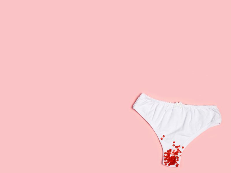 A pair of white underwear with red glitter indicating menstruation on a pink background