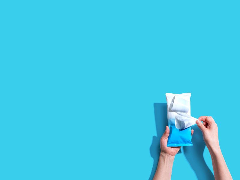 A person's hands holding sanitary wipes on a bright blue surface