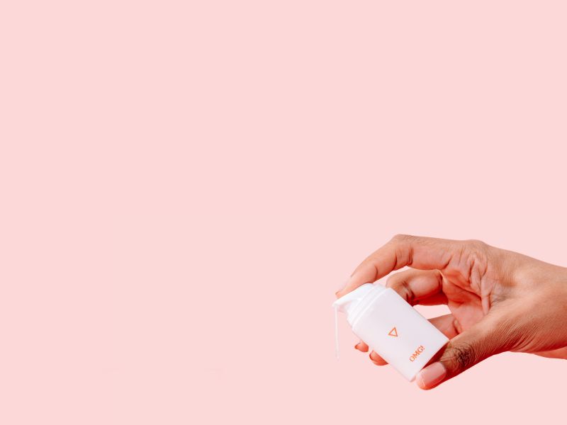 Woman's hand holding a bottle of Wisp OMG Cream over a pink background