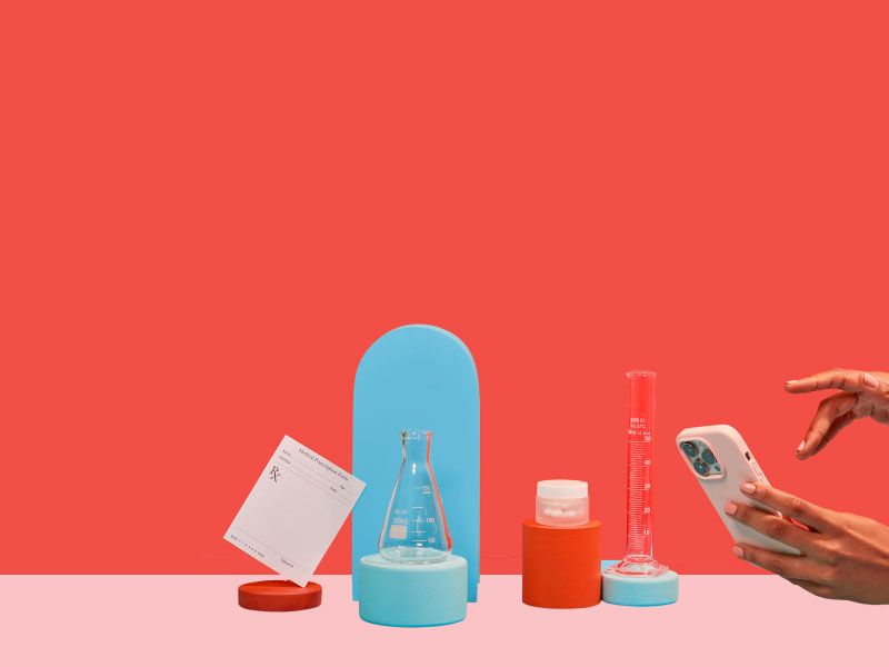 An RX script, testing tubes, and a small Wisp glass pill jar balanced on colorful abstract shapes with hands holding a mobile phone on a light blue surface with a red background