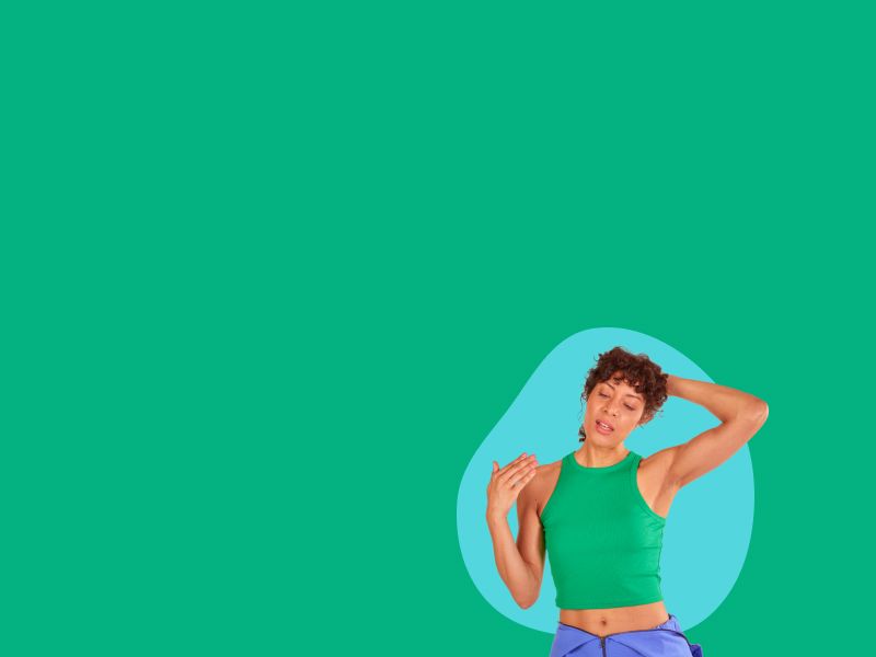 A woman wearing a green tank top is holding her hair up and fanning her face in front of a green background