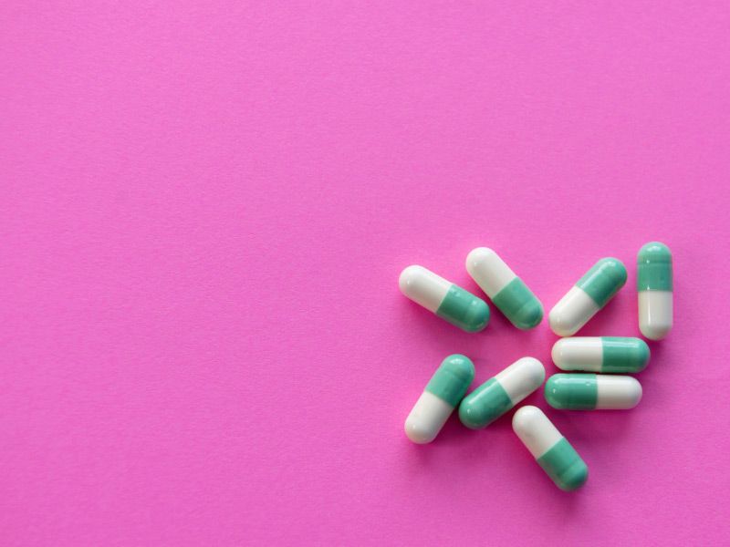 A group of white and green pills on a fuscia surface