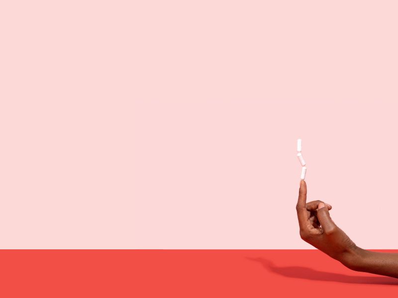 Hand balancing 3 pills on their pointer finger with a pink and red background