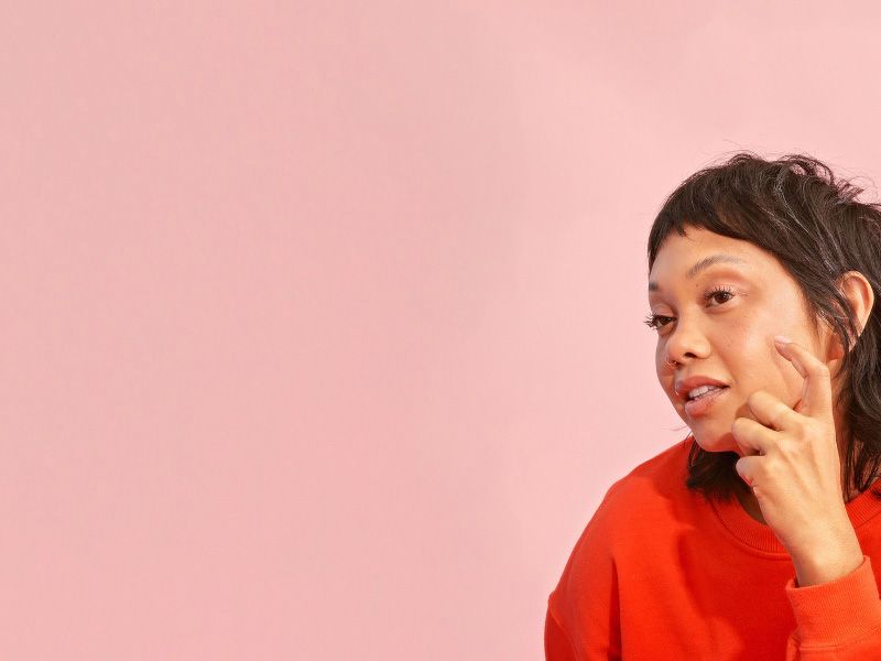 a woman in a red sweater inspecting her skin in a bathroom mirror