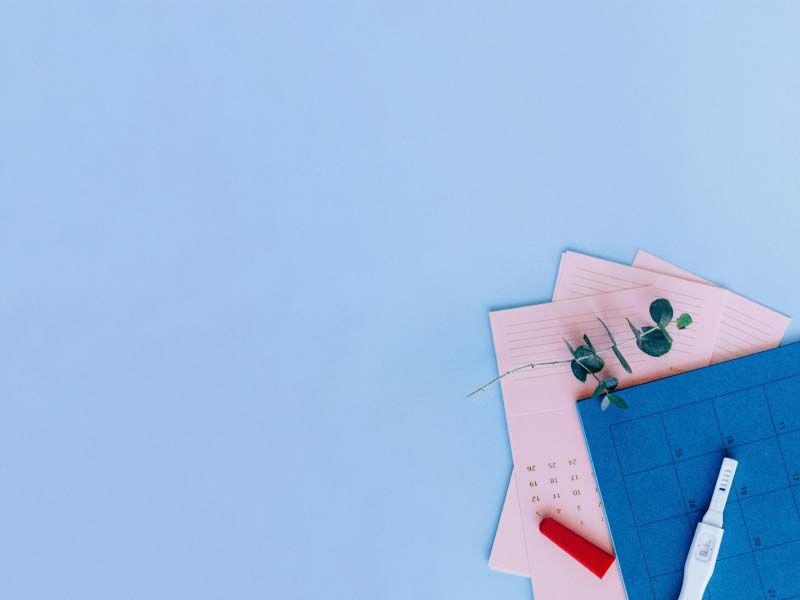 A pregnancy test and a calendar on a light blue surface