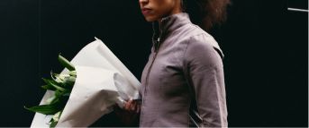 woman walking with jacket and sunglasses on holding a bouquet of flowers wrapped in white paper