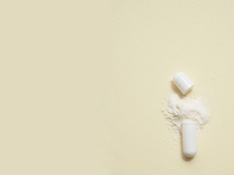 An opened pill capsule with powder spilling out on a light green surface