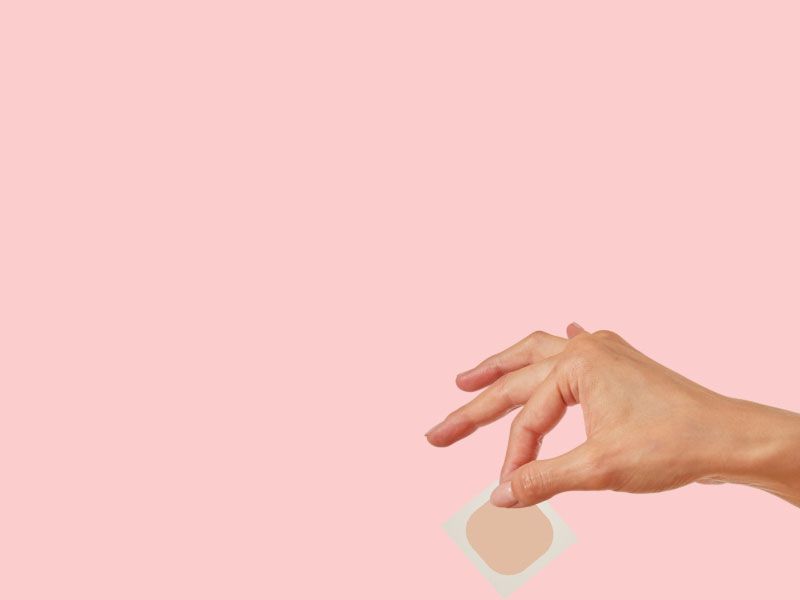 A woman's hand holding a Wisp medication patch with a pink background
