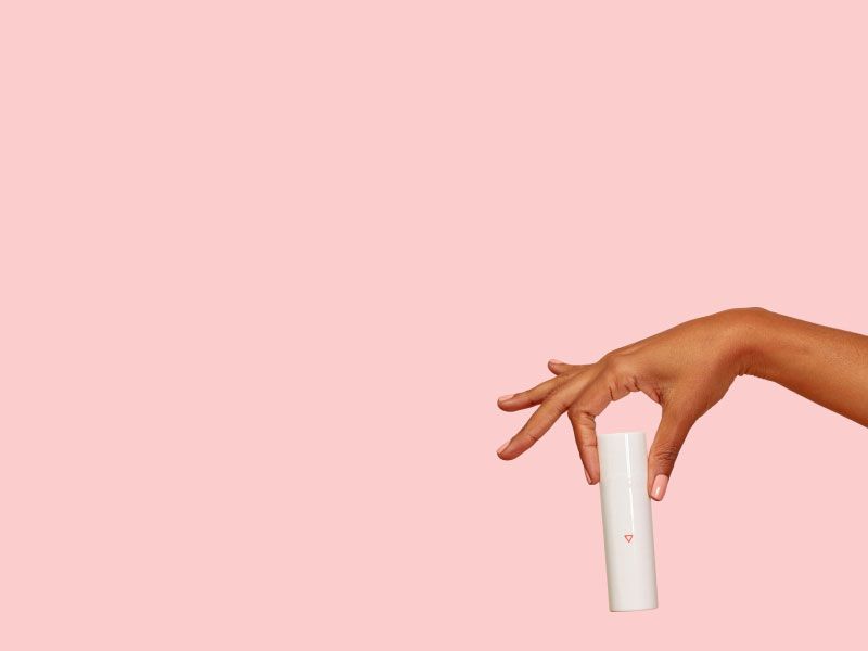 A woman's hand holding a Wisp skincare bottle with a pink background