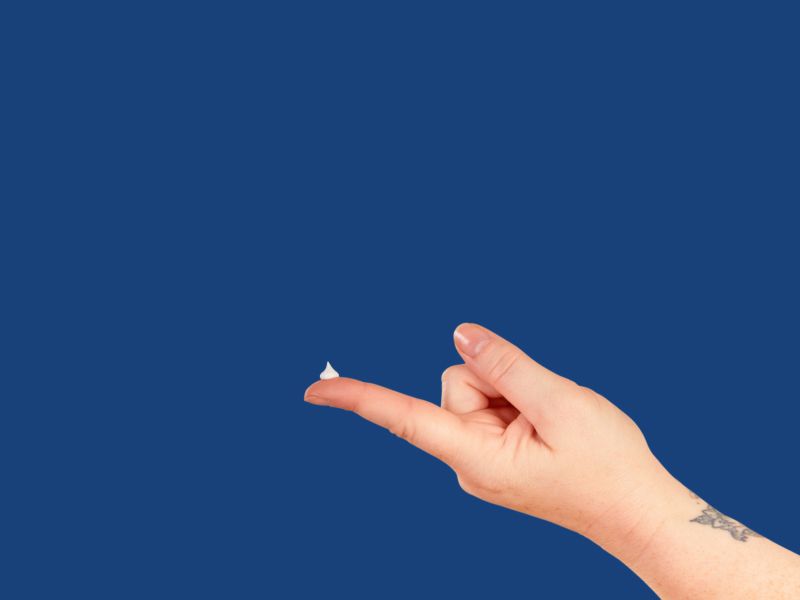 A hand with hemorrhoid treatment on the fingertip on a dark blue background