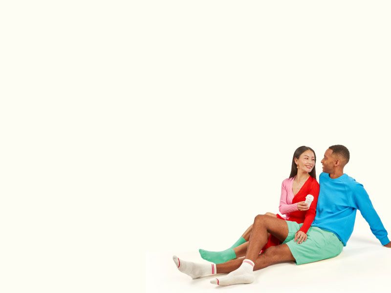 A woman and man sitting on a light yellow surface next and the woman is handing a Wisp pill vial to the man