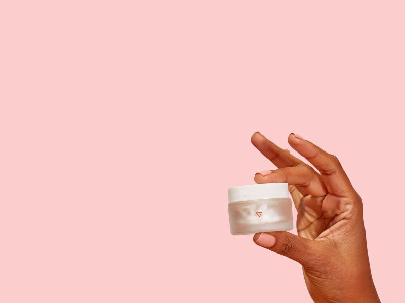 A woman's hand holding a Wisp glass pill jar with a pink background