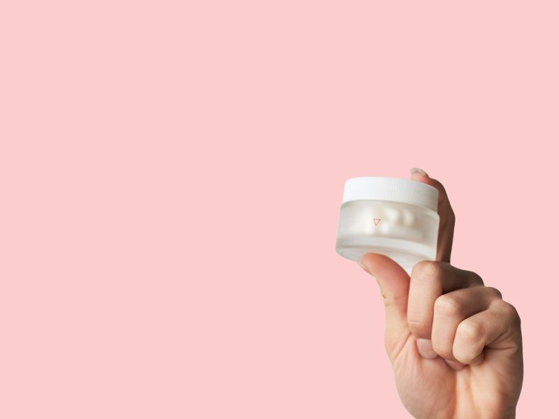 A woman's hand holding a Wisp glass pill jar with a pink background